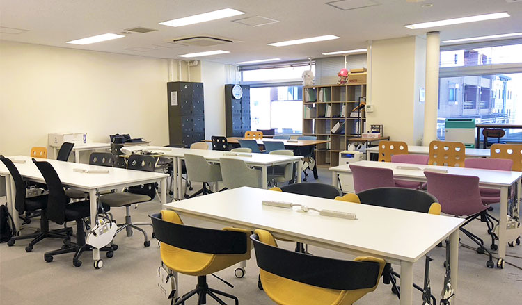 写真：アットジーピージョブトレ横浜の内観写真です。オフィスのような部屋で、長机と椅子がグループごとに並んでいます。ここに全員が集まり、明るい雰囲気のなか、トレーニングをおこなっていきます。